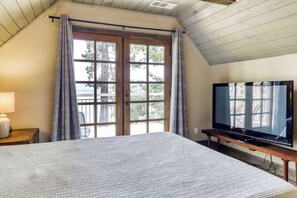 A bedroom with a large bed, a television on a stand, and a window with curtains. - Lakeview Manor (South Lake Tahoe)