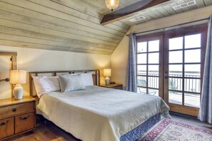 Een slaapkamer met een groot bed, een houten hoofdbord, bedlampen, een nachtkastje, een dressoir met lades en uitzicht door een raam met gordijnen.