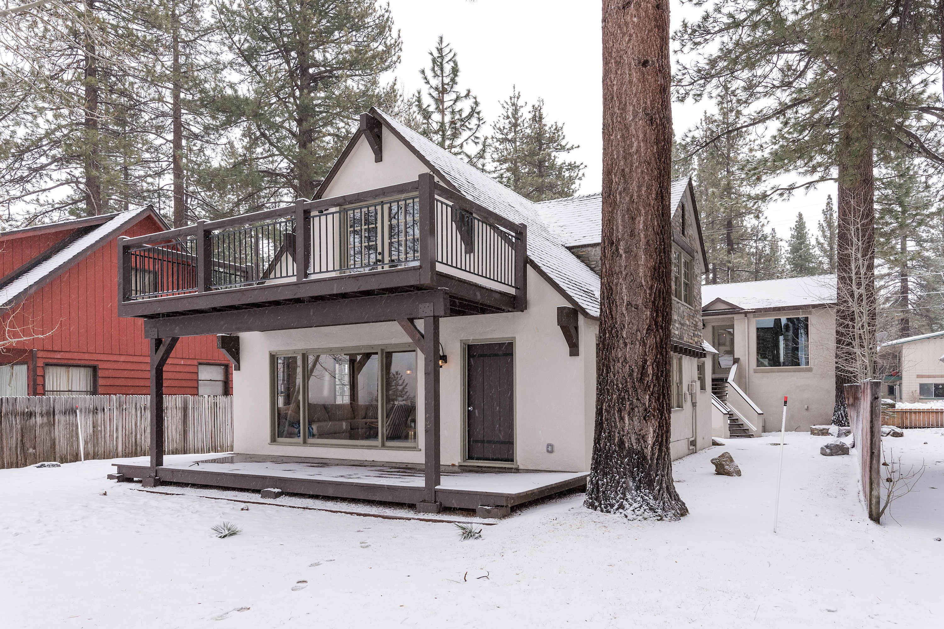 Una casa de dos pisos con balcón, un porche cubierto y un patio cubierto de nieve.