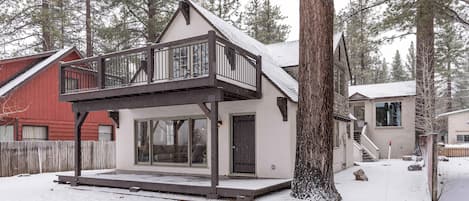 Una casa de dos pisos con balcón, un porche cubierto y un patio cubierto de nieve.