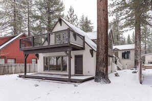 Ein zweistöckiges Haus mit Balkon, überdachter Terrasse und einem schnee bedeckten Garten.