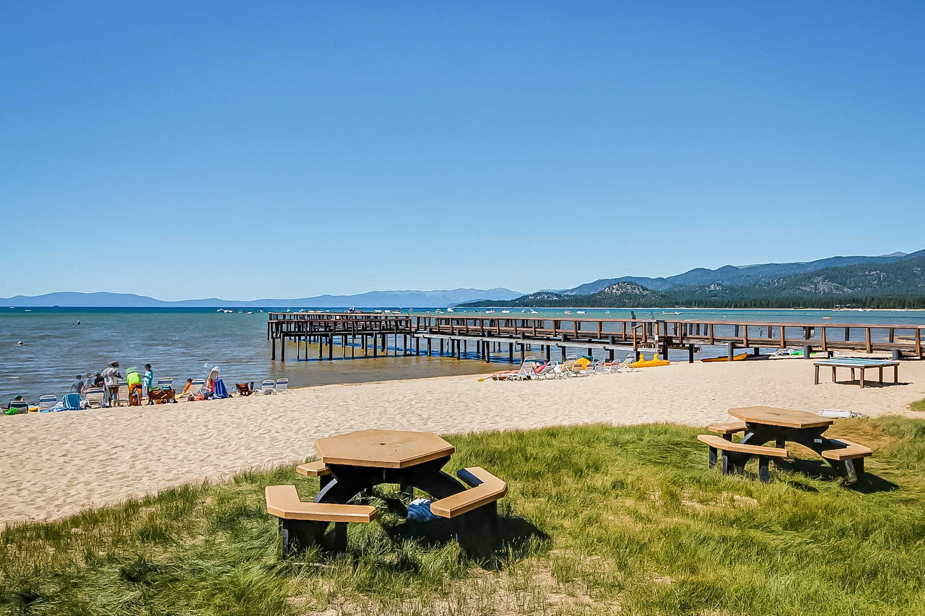 A beach with picnic tables, a wooden pier, and a clear sky.