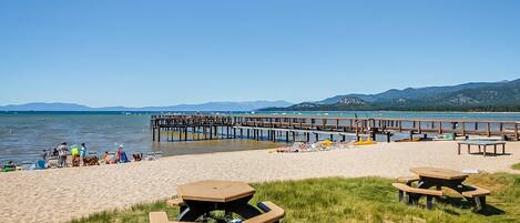 A beach with picnic tables, a wooden pier, and a clear sky.
