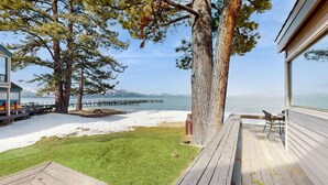 En terrass med utsikt över en strand och en brygga, ett gräsområde och ett stort träd.