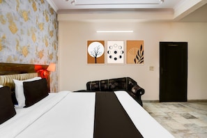 Habitación de hotel con cama, escritorio, silla, lámpara y una obra de arte en la pared.