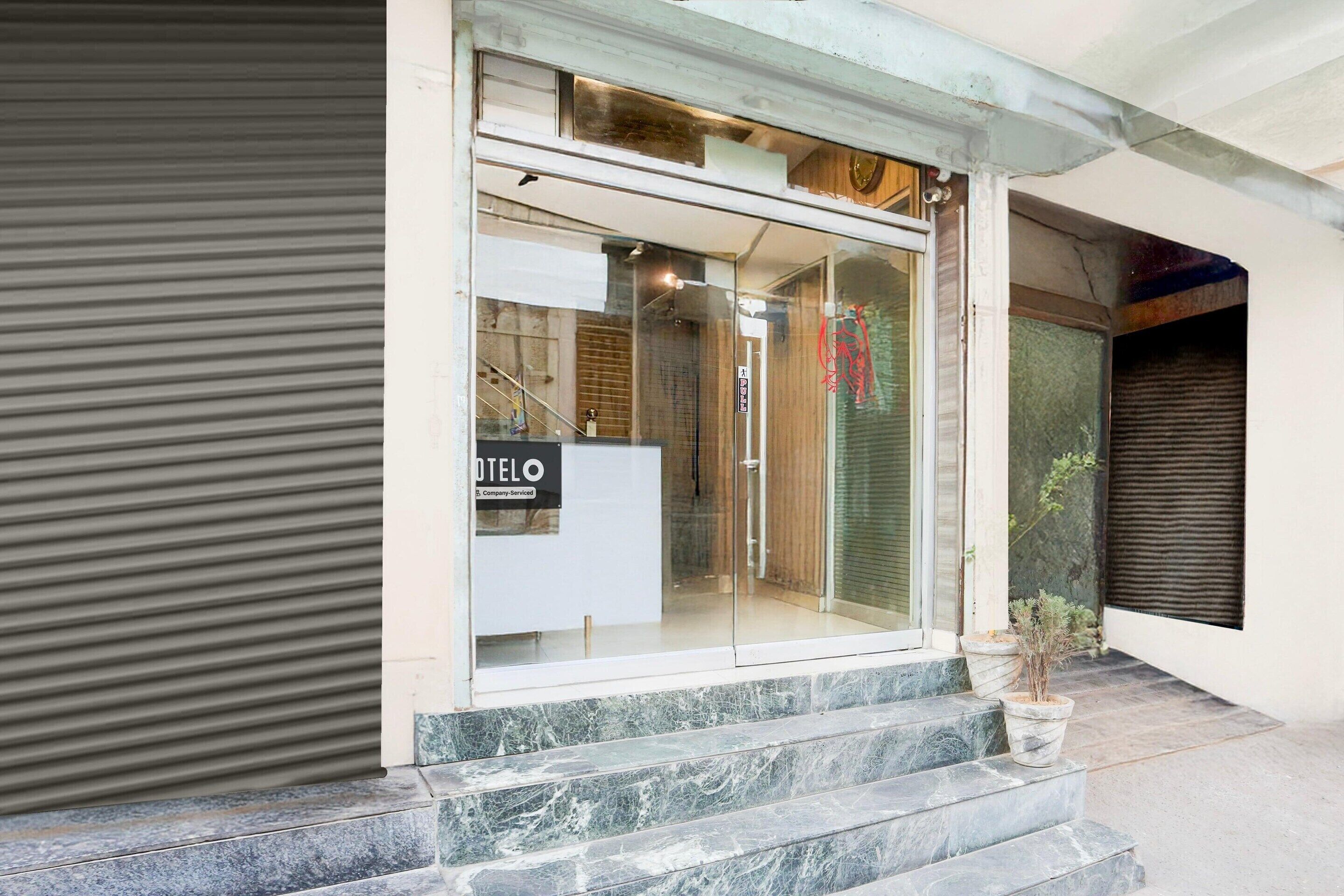 A building entrance with a closed shutter, a signboard, and a potted plant on the steps.