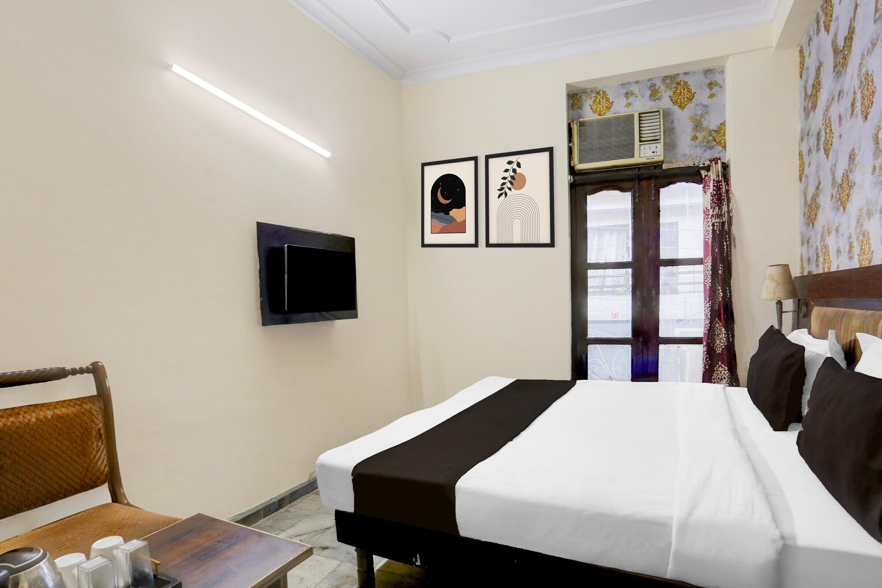Une chambre d’hôtel avec un lit, un téléviseur fixé au mur, une fenêtre avec des rideaux et une table avec une chaise.