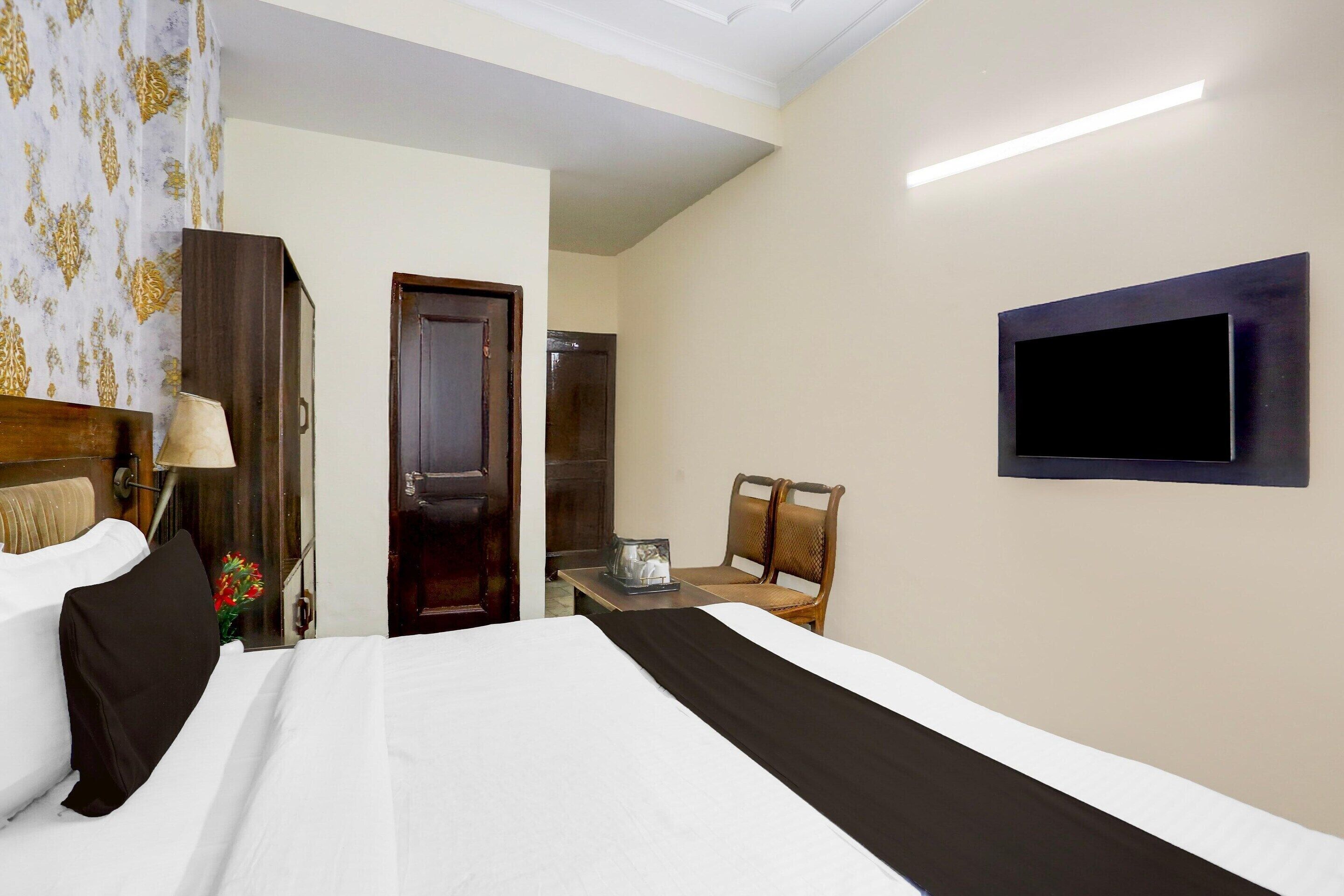 Une chambre d’hôtel avec un lit, un téléviseur fixé au mur, une chaise et un bureau avec une lampe.