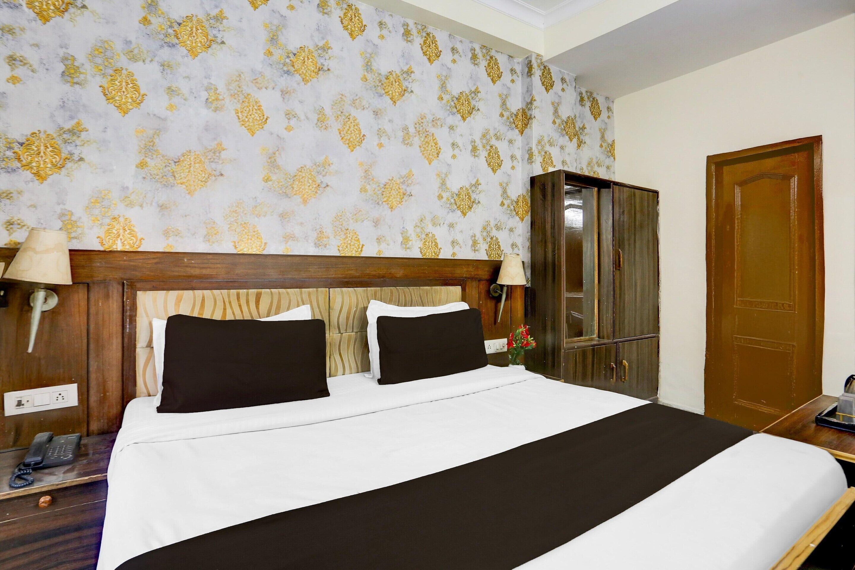 Une chambre d’hôtel avec un grand lit, une tête de lit en bois, une armoire, une table de chevet avec une lampe et un téléphone.