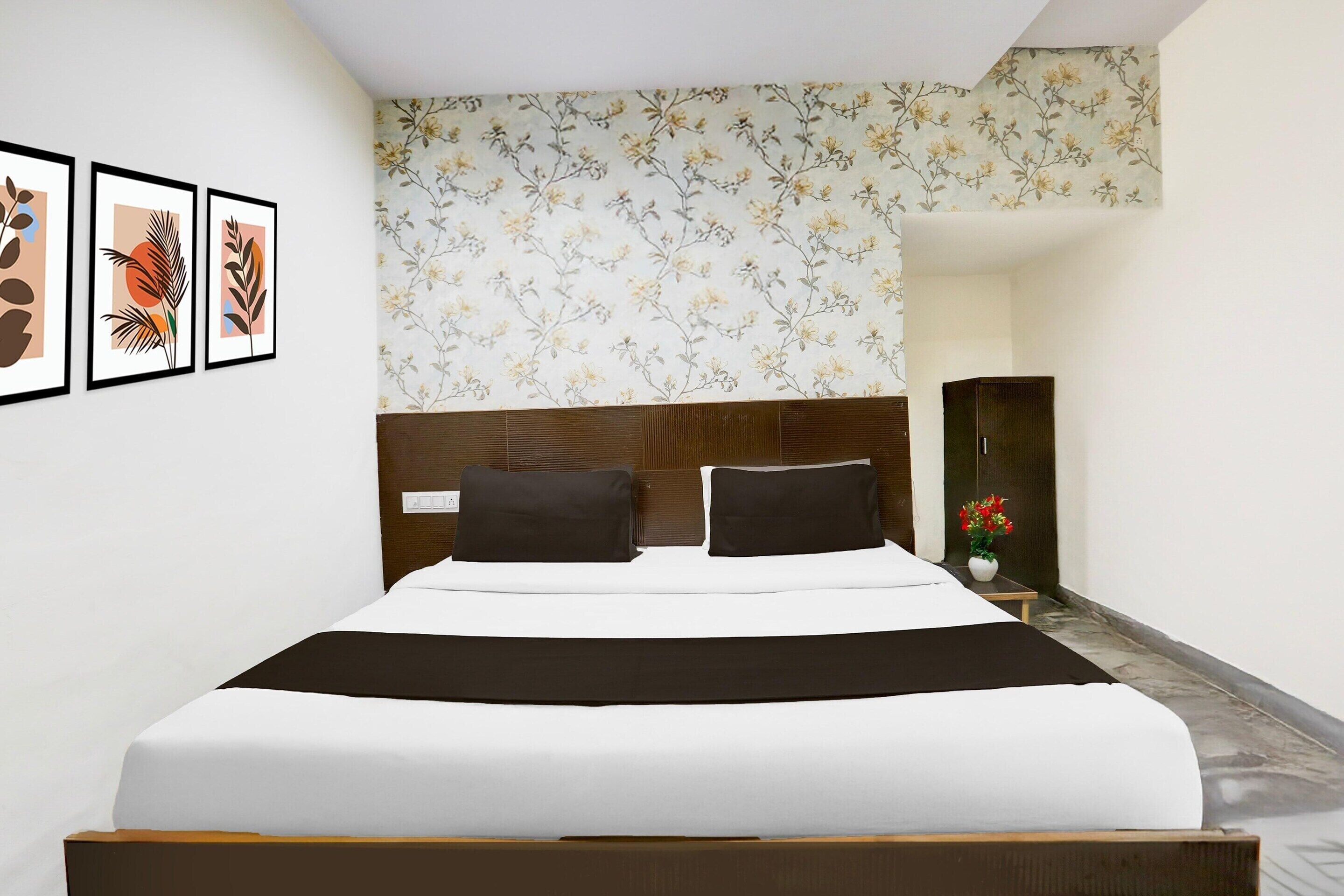 Ein ordentlich bezogenes Bett mit Kopfteil, eine Wand mit Blumenmuster-Tapete und drei gerahmte Bilder.