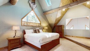 Ein Schlafzimmer mit einem hölzernen Bett, Nachttischen, einem Fenster und einer schrägen Decke.