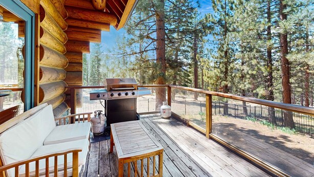 Eine Blockhütte mit einer Terrasse, einem Grill, einer Couch und einem Tisch.