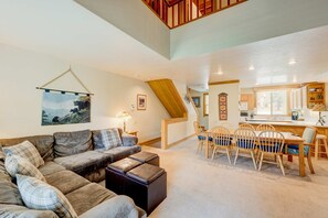 A spacious living area with a sofa, ottoman, and dining table with chairs. A staircase leads to an upper level. - Condo with private balcony, gas fireplace, & washer&dryer (Truckee)