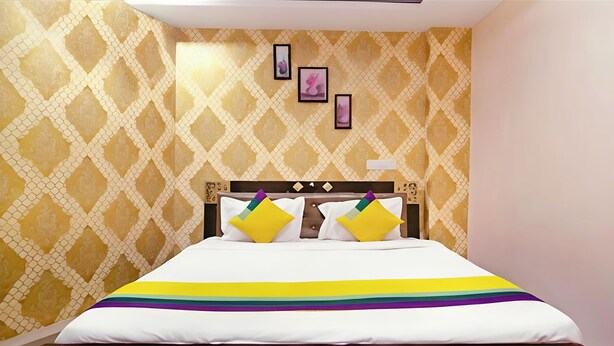A hotel room with a patterned wallpaper, a bed with a rainbow-striped bedspread, and three framed pictures on the wall.