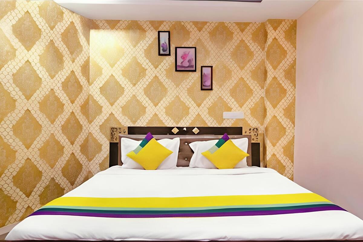Habitación de hotel con papel tapiz estampado, una cama con colcha a rayas de arcoíris y tres cuadros en la pared.