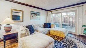 A living room with a sofa, ottoman, lamp, and a large window with a view. - Perfect Lake Retreat W/ Shared Pool, Fast WiFi, Private Patio & Easy Lake Access (Tahoe Vista)