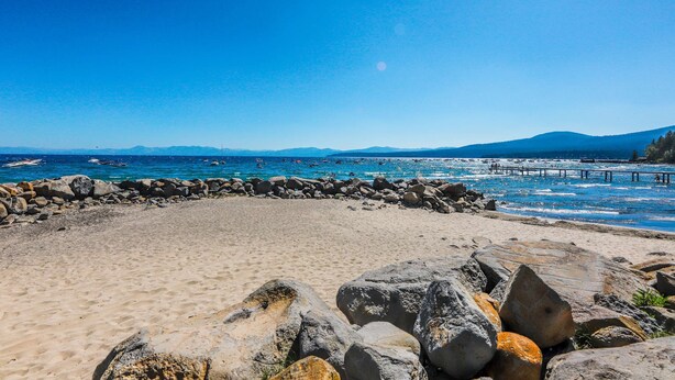 A beach with a rocky foreground, a clear blue sky, and distant mountains. - Perfect Lake Retreat W/ Shared Pool, Fast WiFi, Private Patio & Easy Lake Access (Tahoe Vista)