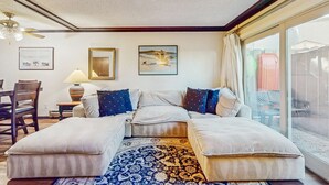 A room with a sofa, ottoman, a lamp, a framed picture, and a view through a window. - Perfect Lake Retreat W/ Shared Pool, Fast WiFi, Private Patio & Easy Lake Access (Tahoe Vista)