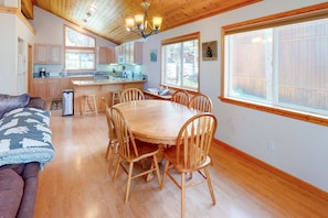 A cozy interior with a wooden dining table, chairs, a sofa, and a kitchen area with wooden cabinets and a large window. - Escape to Mountain Comfort in the Heart of Truckee, CA (Truckee)