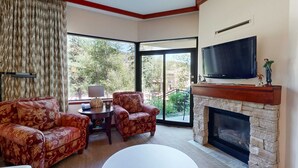 A living room with a fireplace, a television, and a large window with a view of trees. - Everline Resort & Spa adjoining condos with pool, hot tub, ski-in&ski-out locale (Olympic Valley)