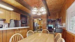 L’intérieur d’un chalet en bois comprend une table à manger, des chaises, un coin cuisine et un salon avec un téléviseur.