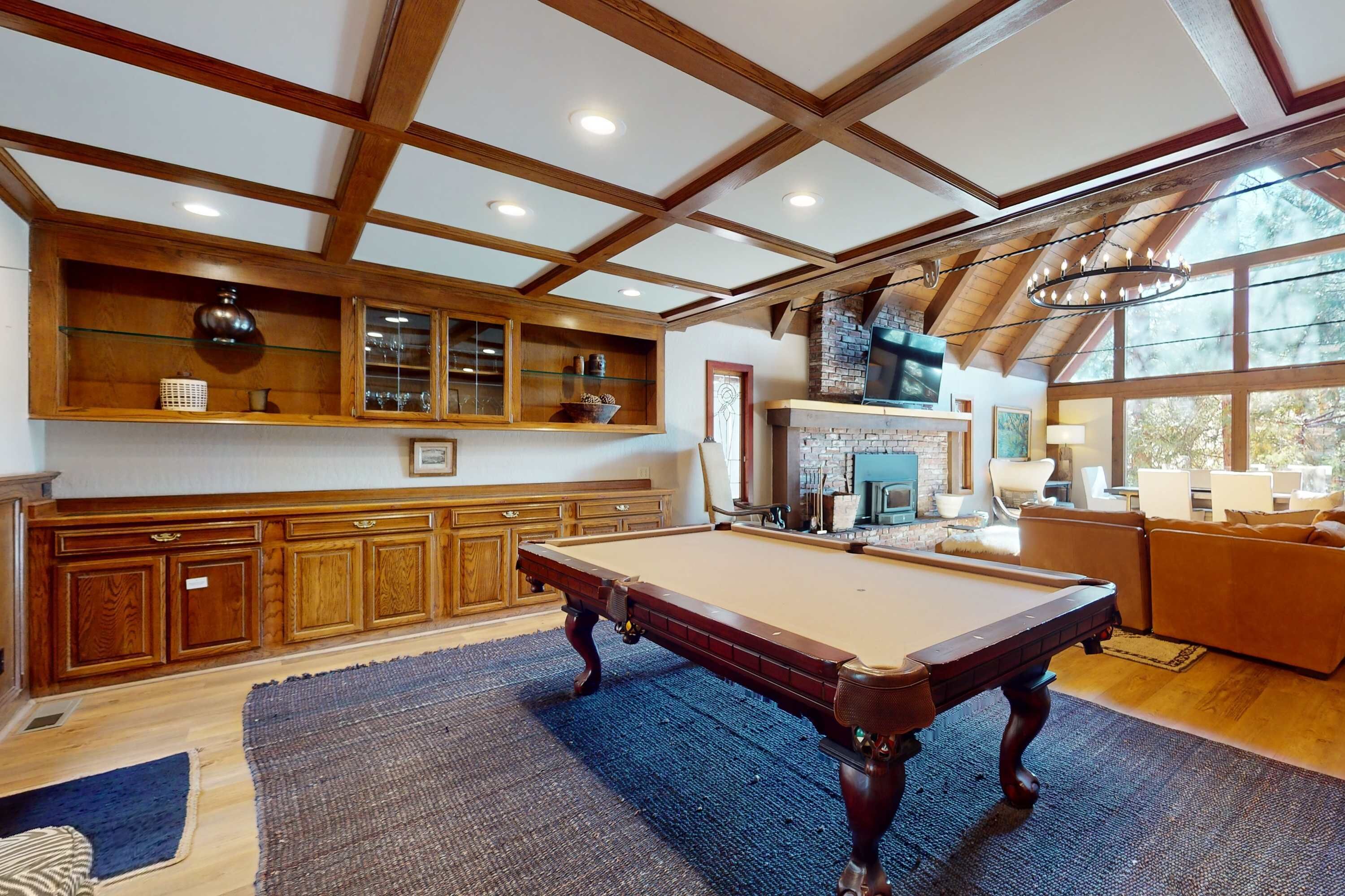 Une table de billard dans une pièce dotée de meubles en bois, d’une cheminée et d’une grande fenêtre.