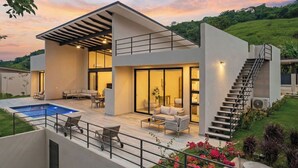 Une maison moderne à deux étages dotée d’une piscine, d’un espace salon extérieur et d’un escalier.
