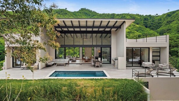 Une maison moderne dotée d’une piscine, d’un espace salon extérieur et offrant une vue sur une colline verdoyante.