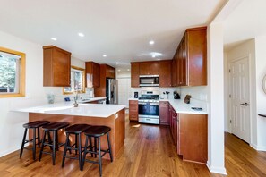 A modern kitchen with wooden cabinets, a central island with stools, a stainless steel refrigerator, and a built-in oven. - Charming cabin near downtown Truckee & skiing with large deck (Truckee)
