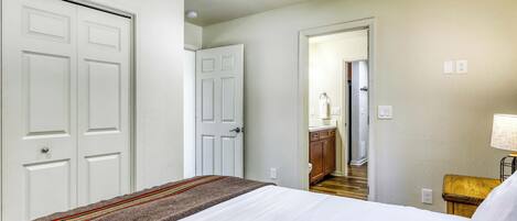 A bedroom with a bed, a door, a hallway, and a bathroom visible through an open door.