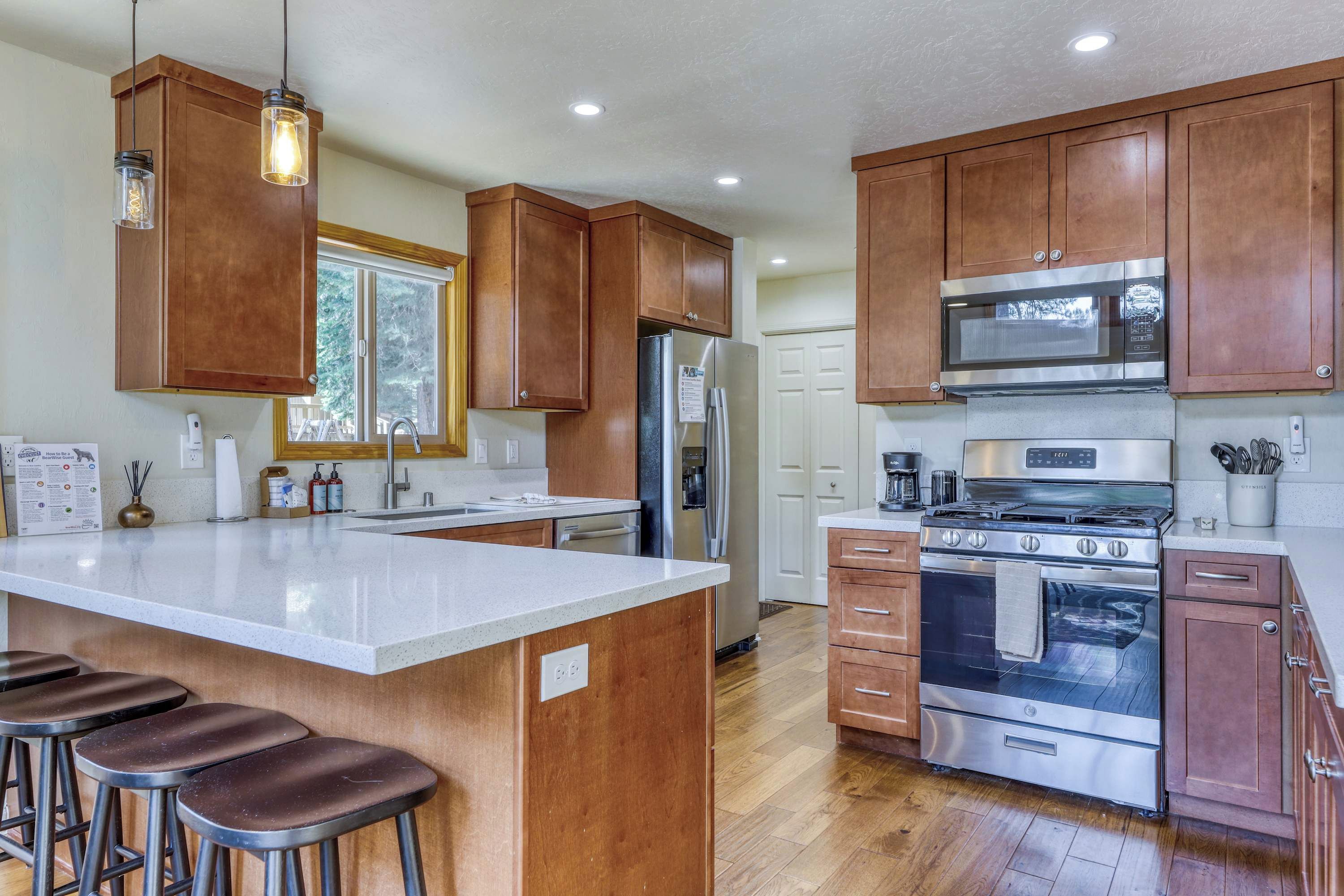 A kitchen with wooden cabinets, stainless steel appliances, a large island with stools, and a window providing natural light.