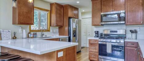 A kitchen with wooden cabinets, stainless steel appliances, a large island with stools, and a window providing natural light.