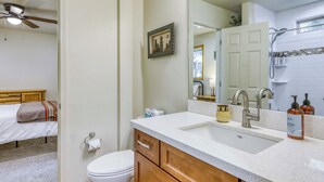 Un baño con inodoro blanco, muebles de madera, lavabo con espejo y zona de ducha.