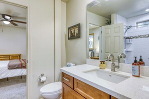 A bathroom with a white toilet, wooden cabinets, a sink with a mirror, and a shower area. - Charming cabin near downtown Truckee & skiing with large deck (Truckee)