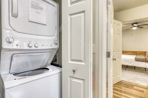 Un lavadero con lavadora y secadora de carga frontal, una puerta con un aviso para el servicio de limpieza, y un dormitorio con cama y ventilador de techo.