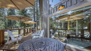 Terraza exterior con mesas y sillas, rodeada por paredes de vidrio que ofrecen vistas a árboles.