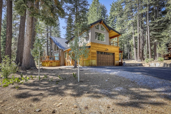 A two-story wooden cabin with a garage, surrounded by tall pine trees. - Charming cabin near downtown Truckee & skiing with large deck (Truckee)