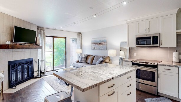 A modern kitchen with a large island, built-in microwave, oven, and a flat-screen TV mounted above the fireplace. - Mountain Condo with  Shared Hot Tub & Pool, High-Speed WiFi, & Private washer & dryer (Park City)