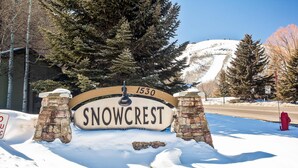 A snow-covered sign with 'SNOWCREST' and the number '1530' in a rural setting with trees and a mountain in the background. - Mountain Condo with  Shared Hot Tub & Pool, High-Speed WiFi, & Private washer & dryer (Park City)