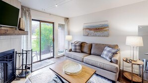 A modern living room with a sofa, a fireplace, a television, and a large window. - Mountain Condo with  Shared Hot Tub & Pool, High-Speed WiFi, & Private washer & dryer (Park City)