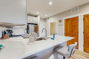 Una cocina moderna con armarios blancos, un refrigerador de acero inoxidable, un lavamanos y una zona de bar con dos taburetes.