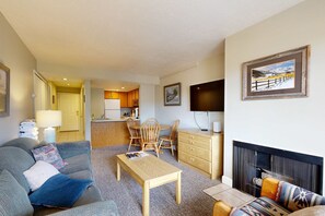 A living room with a sofa, coffee table, fireplace, and a kitchen area in the background. - Mountain-view condo with fireplace, near skiing & main street, on shuttle route (Park City)