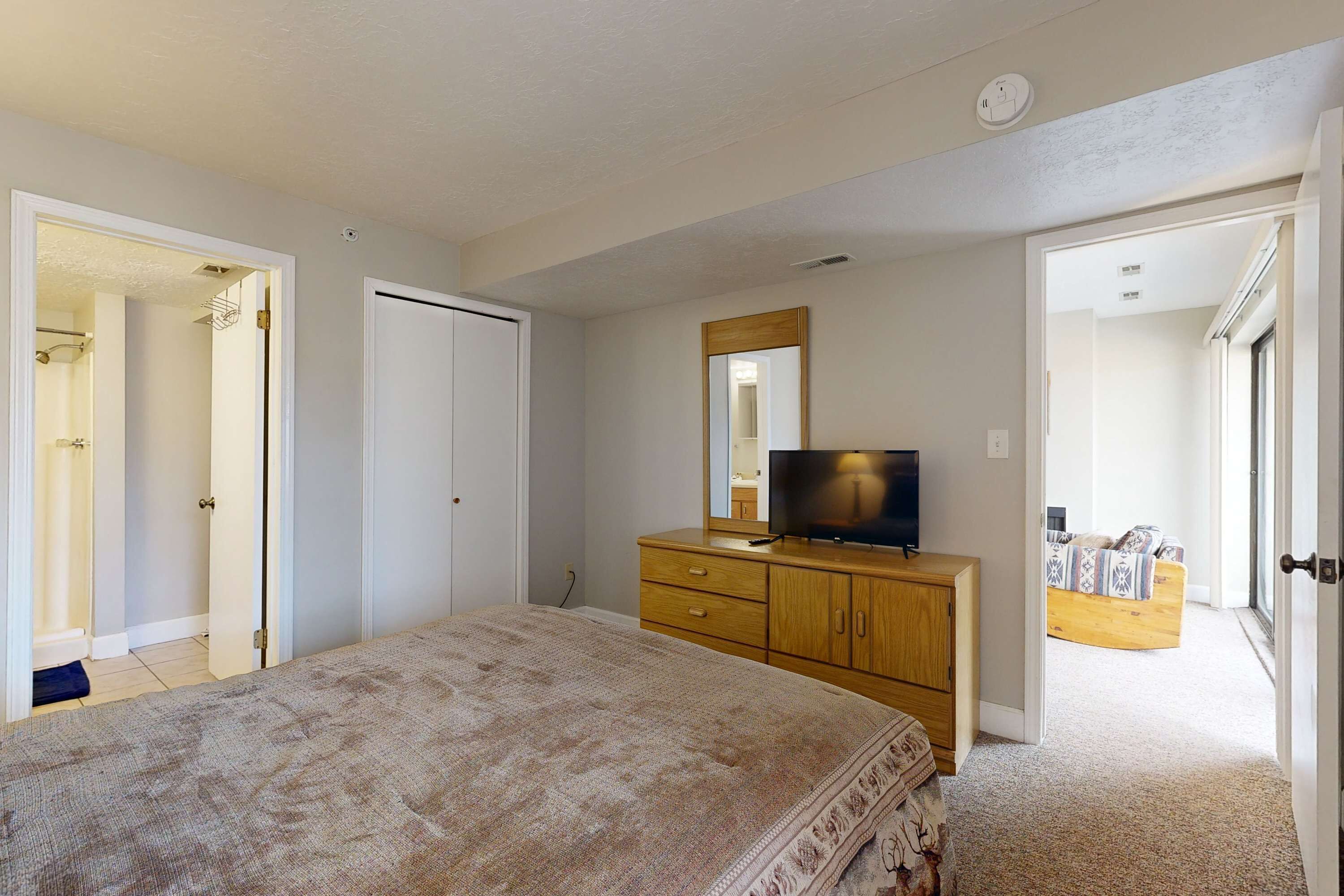 A bedroom with a bed, a dresser, a television, and a mirror. There are doors leading to other rooms.