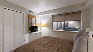 Un dormitorio con cama, cómoda, televisor, ventana con vista y puerta.