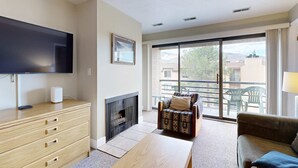 Una sala de estar con televisor de pantalla plana, chimenea, sofá y balcón con mobiliario exterior.