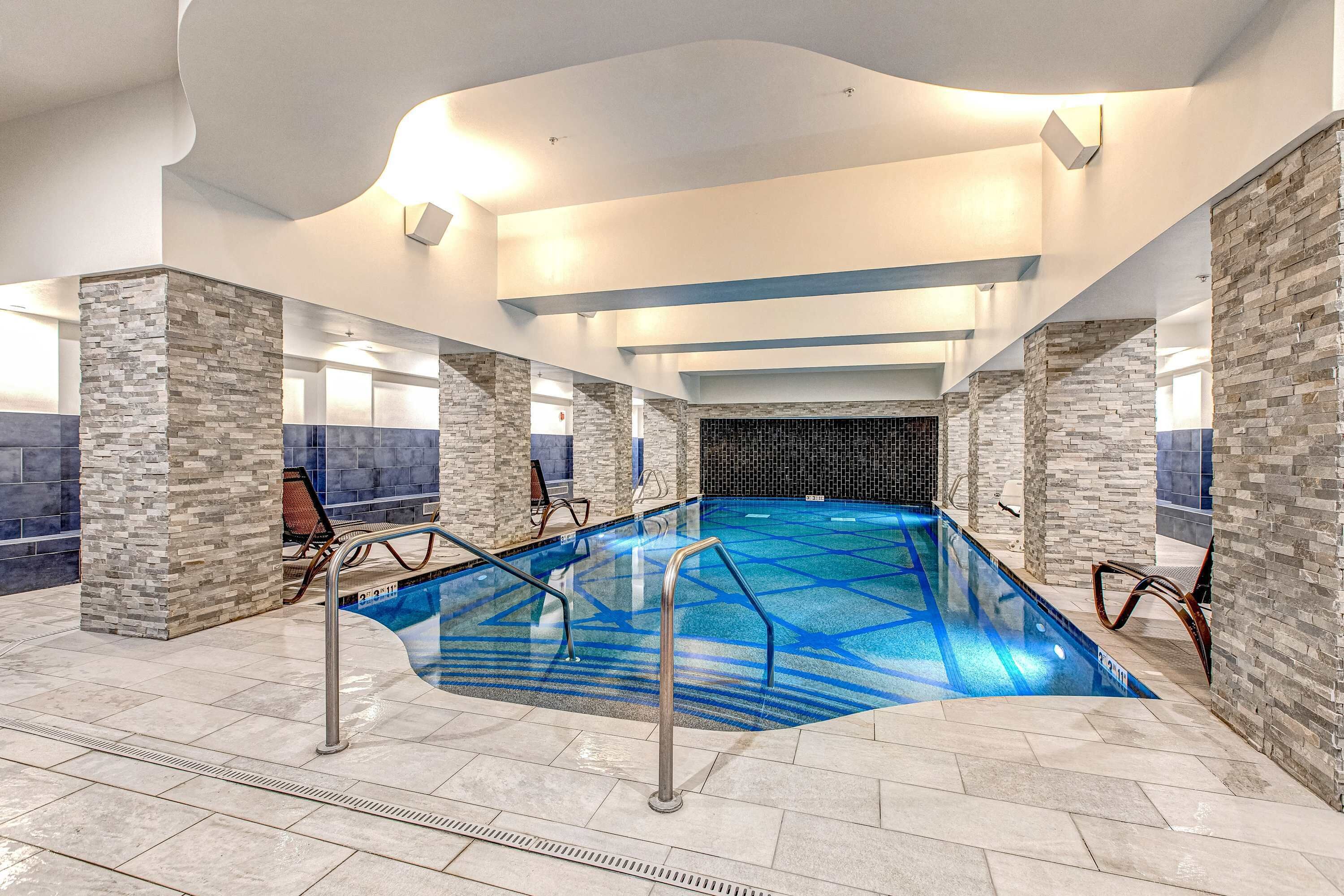 An indoor swimming pool with stone walls, metal railings, and tiled flooring.
