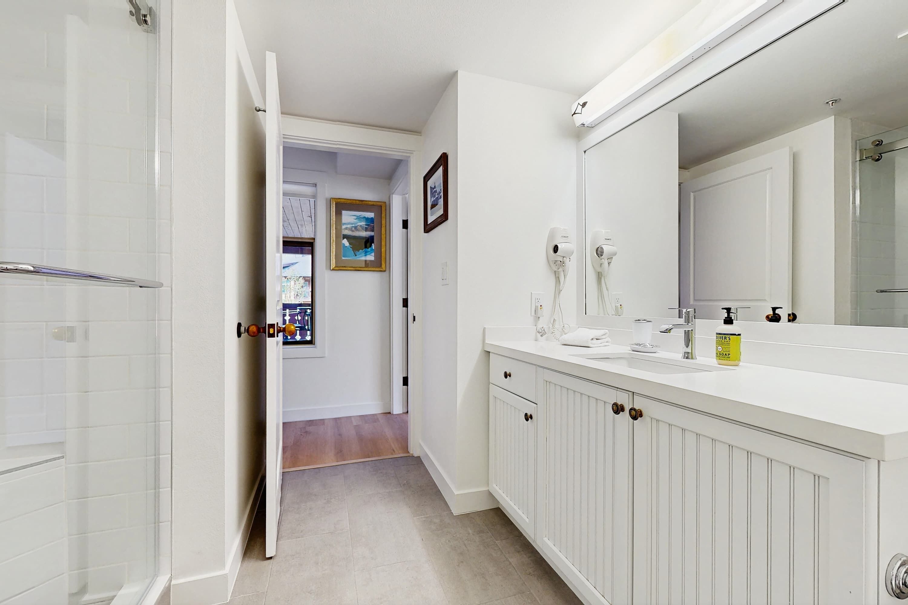 A bathroom with a shower, a sink with a mirror, and a door leading to another room.