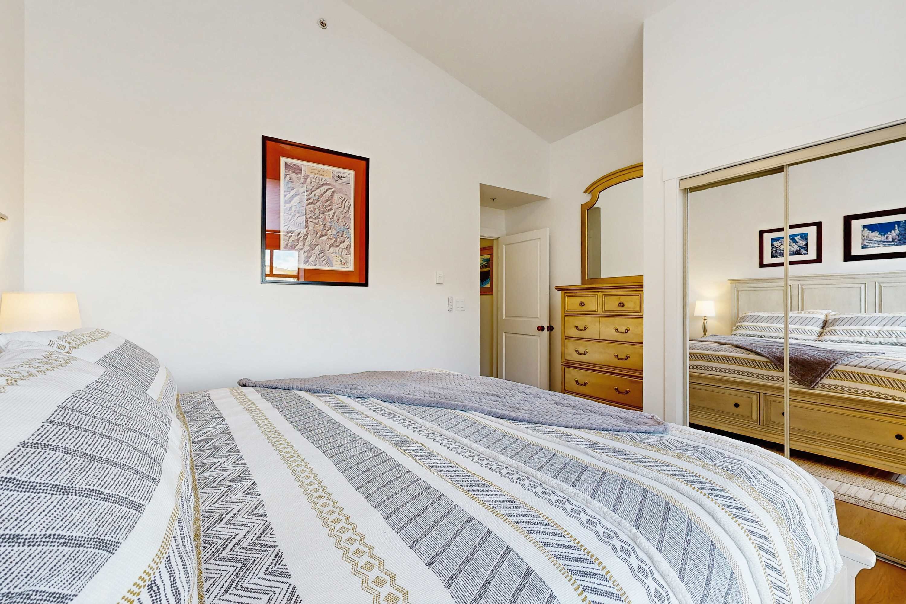 A bedroom with a bed, a dresser, a mirror, and a framed picture on the wall.