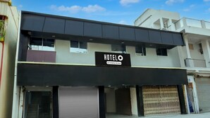 A hotel with a sign indicating it is company-serviced, featuring a modern architectural design with a flat roof and a balcony on the upper floor.
