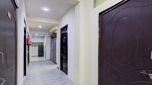 A hallway with a tiled floor, a dark wooden door on the right, and a closed metal shutter door on the left.